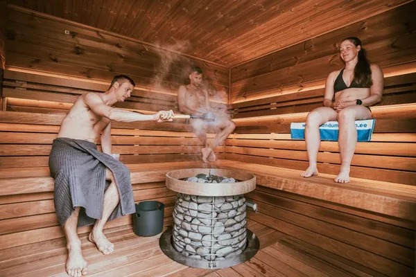 Man pouring water on sauna stones while a woman relaxes