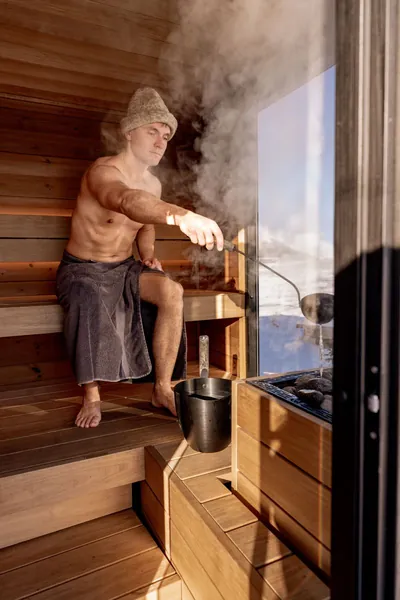 Man pouring water over hot sauna stones