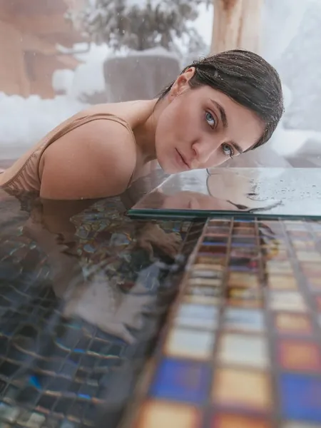 Woman resting calmly at the edge of a snow-surrounded plunge pool