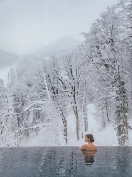 Woman floating in an infinity pool framed by snowy trees