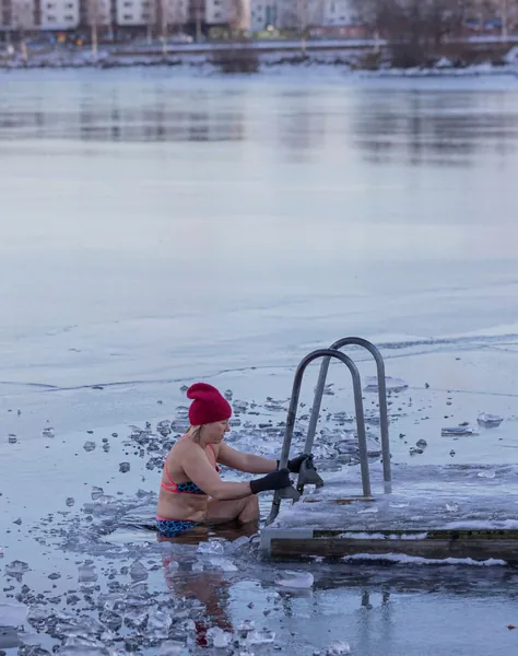 Woman in a red hat stepping into icy lake water