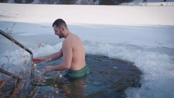 Man lowering himself into icy water at a ladder