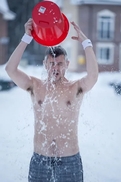 Man pouring a bucket of ice water over himself in the snow